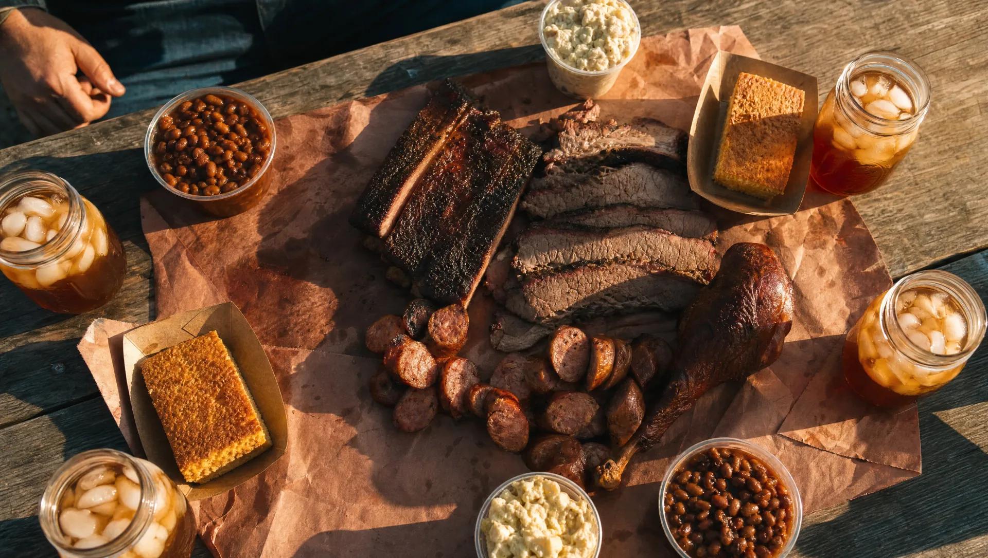 Family-style BBQ spread on butcher paper on a picnic table